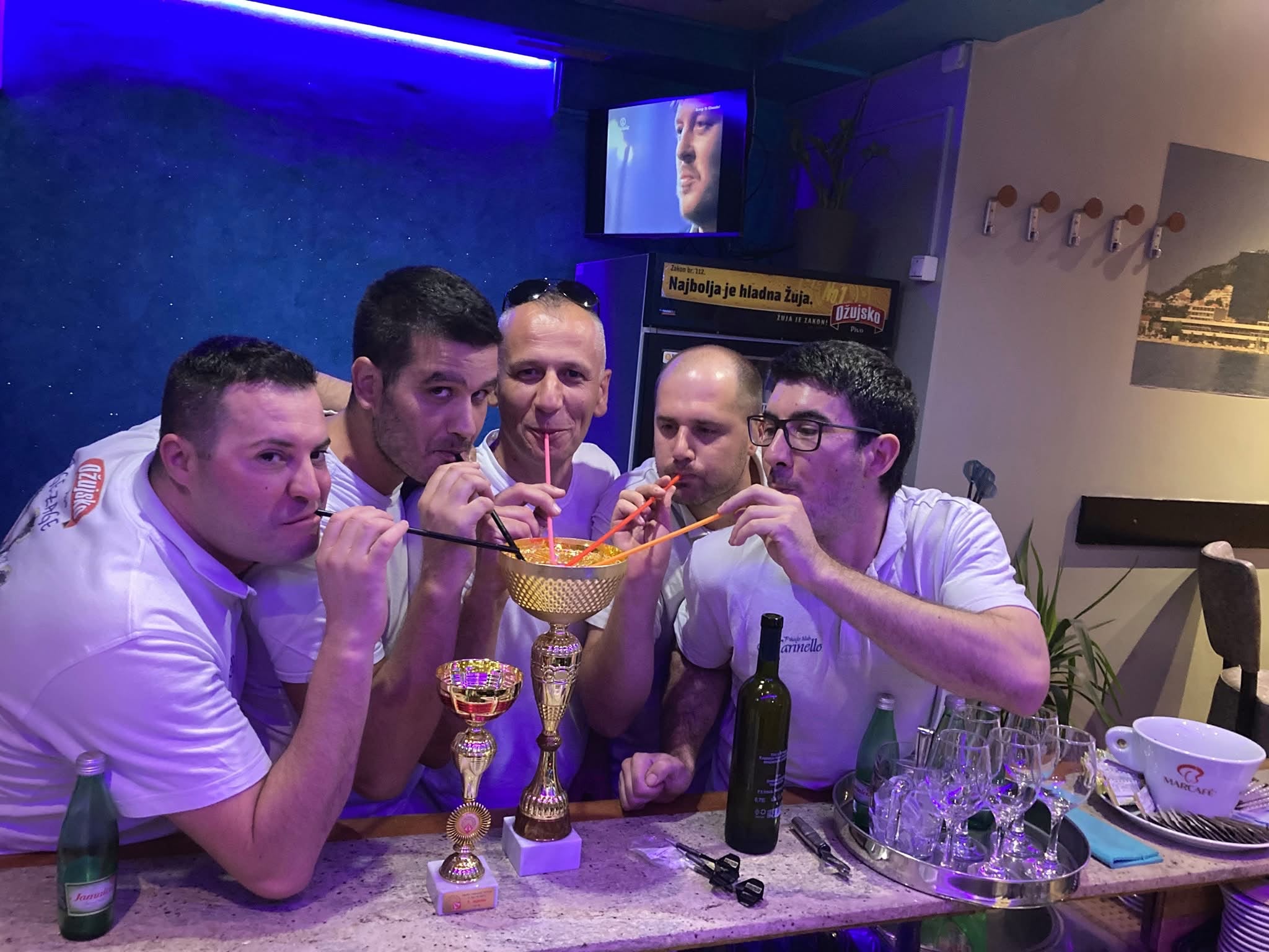 Petorica igrača piju iz pehara na slamke za šankom